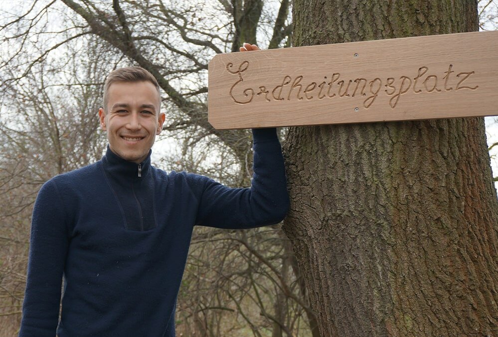 Mitarbeiter Jan neben einem neuen angebrachten Schild auf einem Erdheilungsplatz