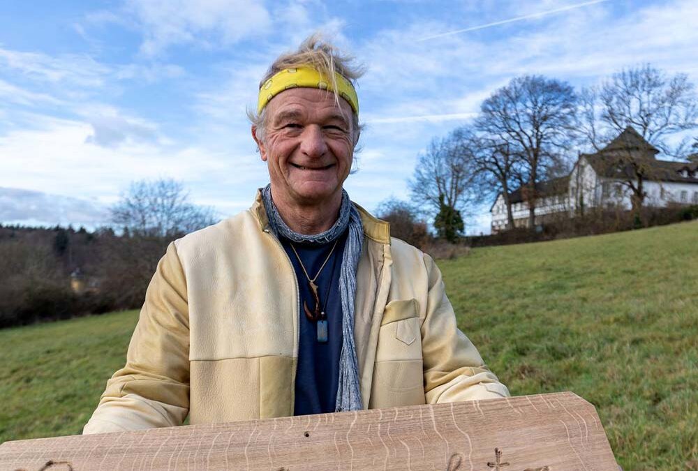 Tilo Hildebrandt zeigt auf einer Wiese unterhalb der Villiper Windmühle ein Schild, das die zukünftigen wieder naturnah umgestalteten Flächen als Erdheilungsplätze ausweist.