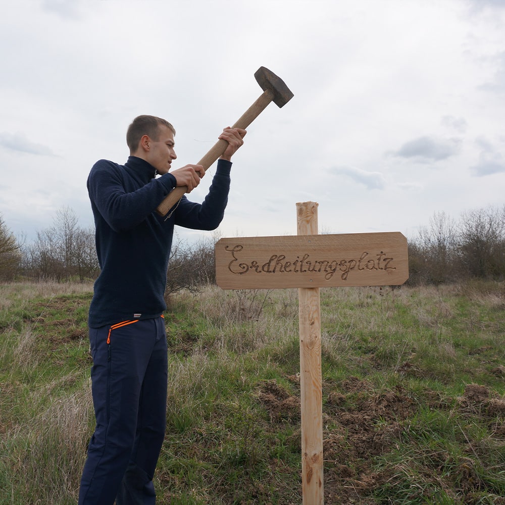 Mitarbeiter Jan bringt auf dem Erdheilungsplatz Dardesheim ein Schild an