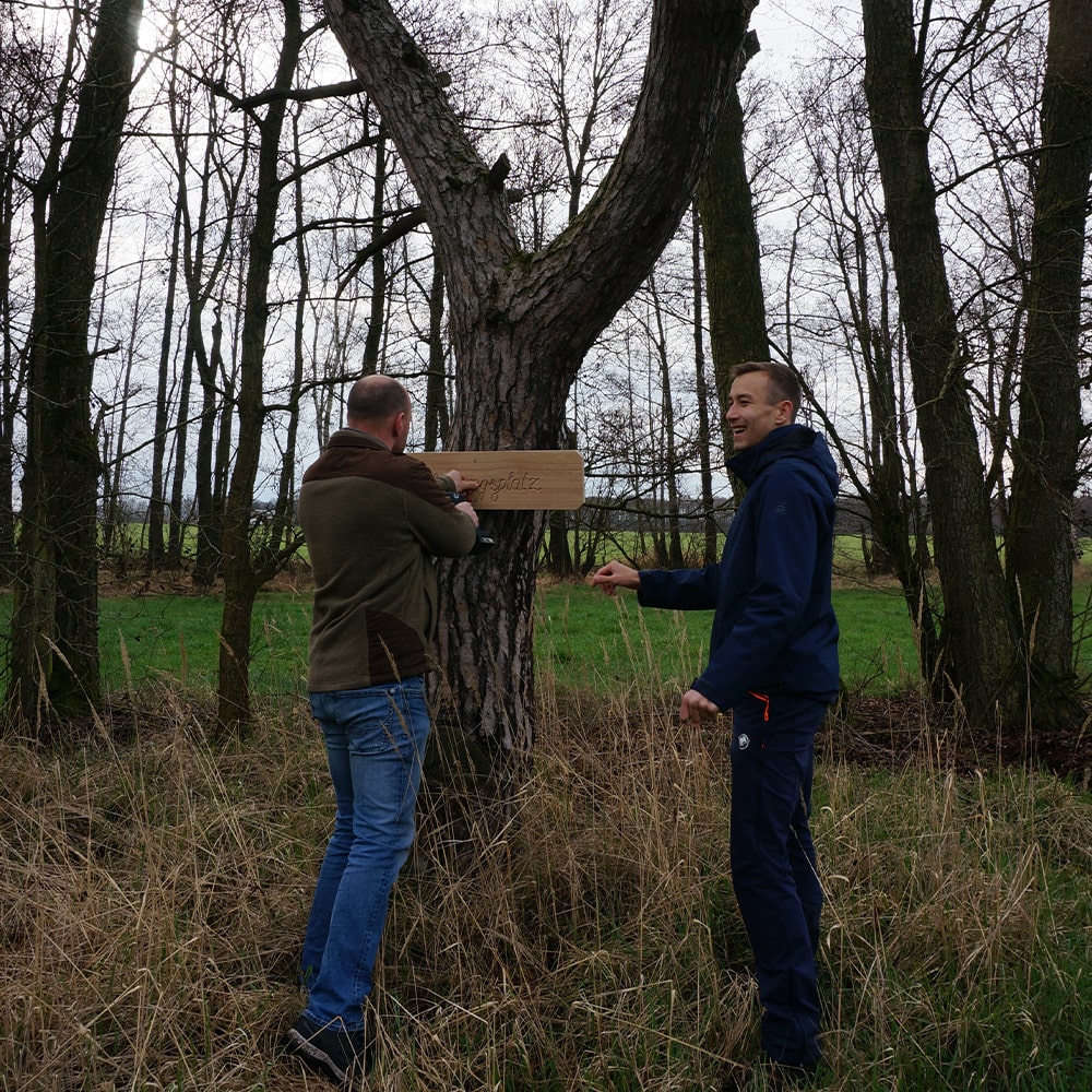 Mitarbeiter Jan und Vorstandsmitglied Raimar bringen am Erdheilungsplatz Luko Gruenland ein Schild an