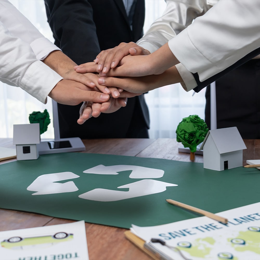 Mehrere Unternehmer legen über einem Tisch mit einem Recycling-Zeichen die Händer aufeinander